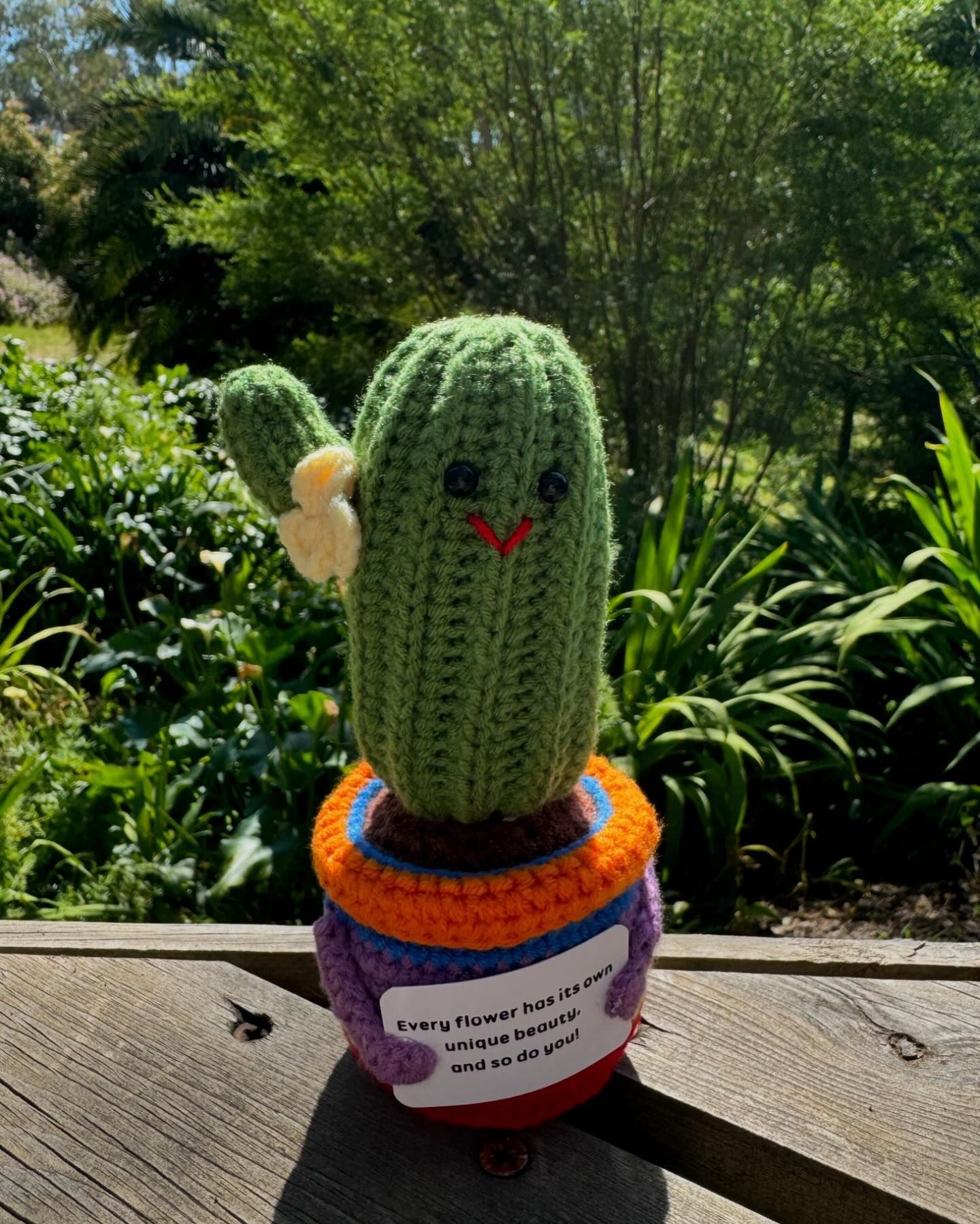 Crocheted cactus with flower in colorful pot, outdoors on a sunny day.